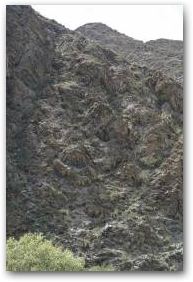 Склон горы, где слоистые выходы скал покрыты чёрными натёками особенно густо.